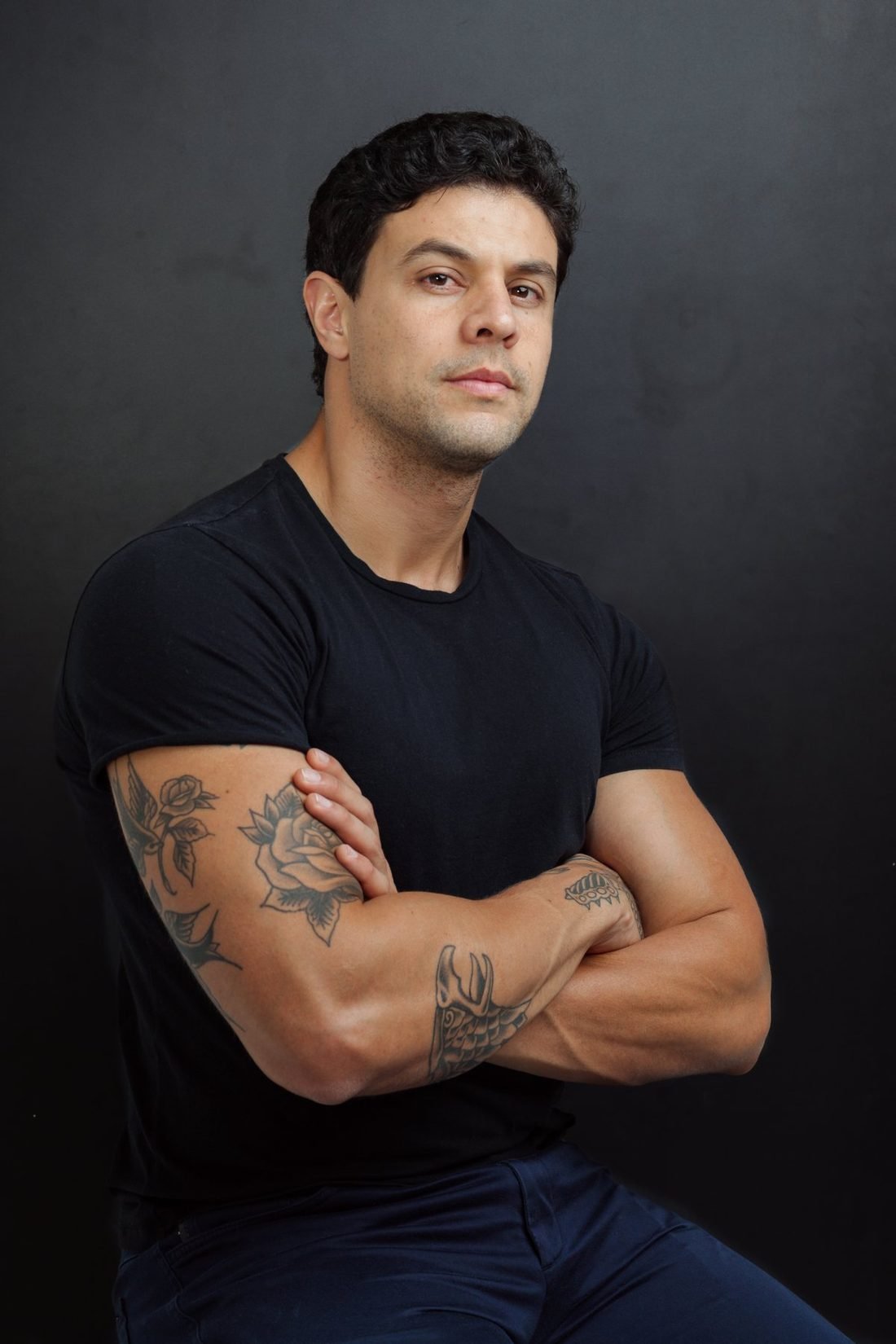 Luan Oliveira, de braços cruzados, em fundo escuro